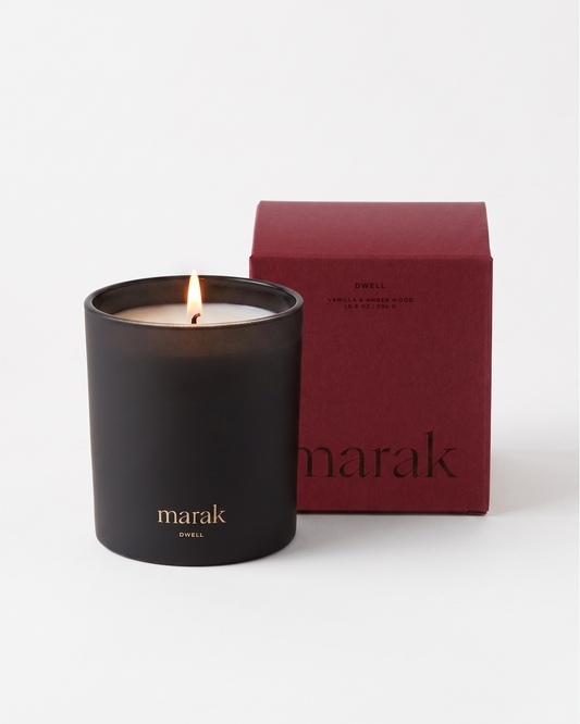 Marak candle in black jar with flame next to maroon Vanilla & Amber Wood gift box