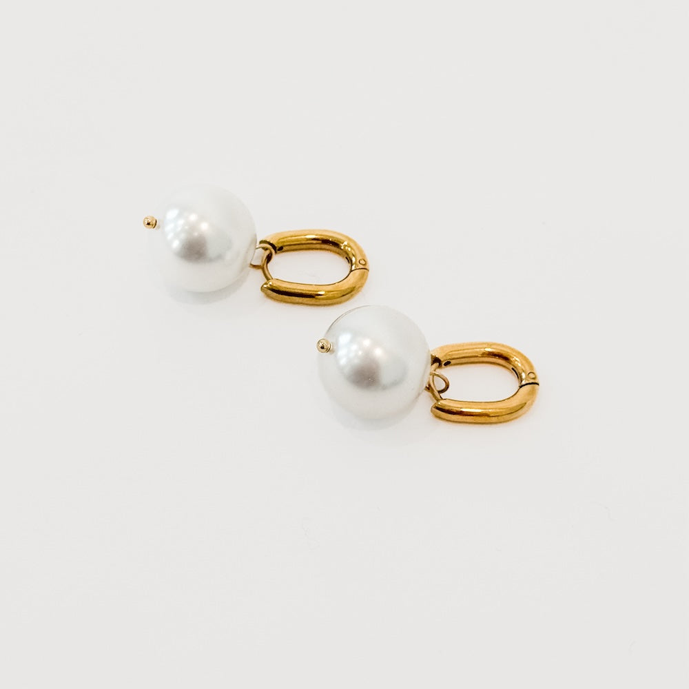 Gold-tone huggie hoops with white pearl drops, close-up angled view