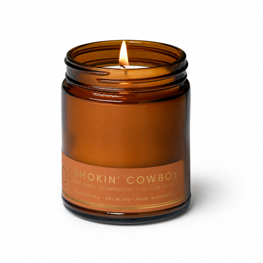 Amber-brown glass candle jar with 'Smokin' Cowboy' label and a centered burning wick