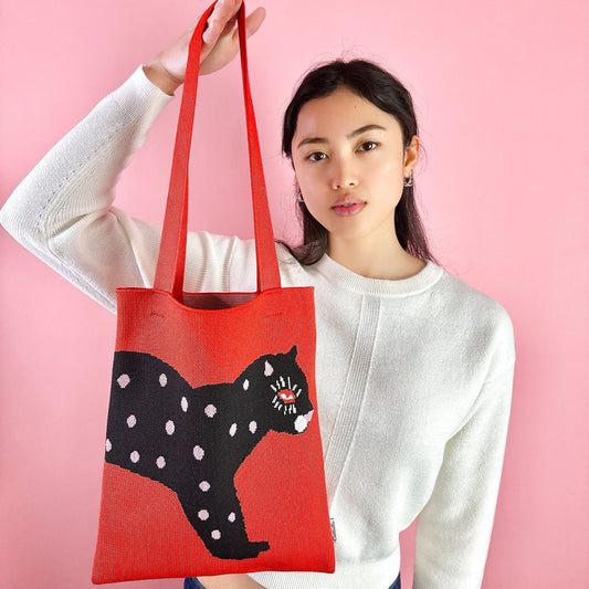 Red knit tote bag with black polka-dot cat graphic and carry handles.