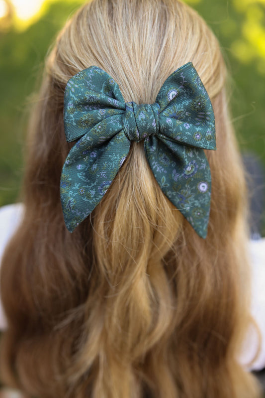 Hair bow on blond hair, dark teal floral patterned bow with tied center knot