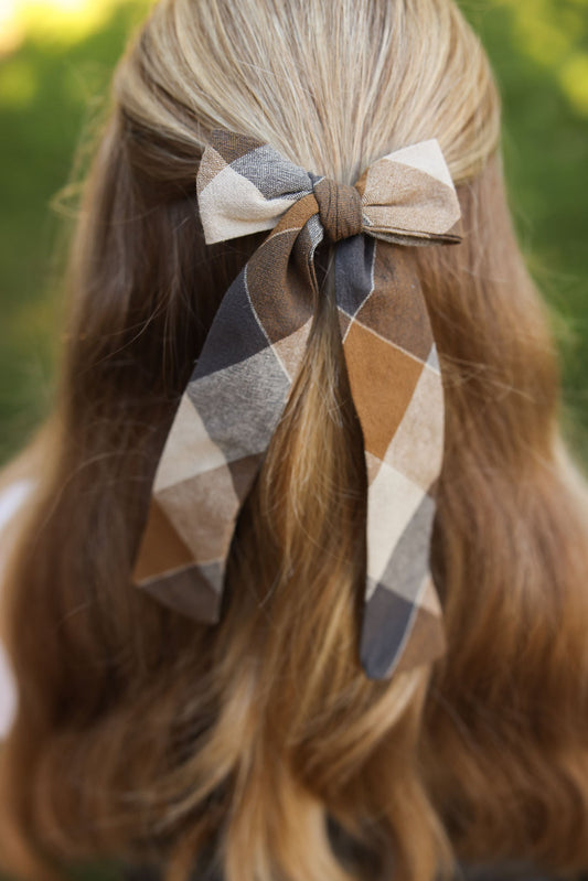 Plaid hair bow on model’s hair, tan, gray, and cream diamond pattern