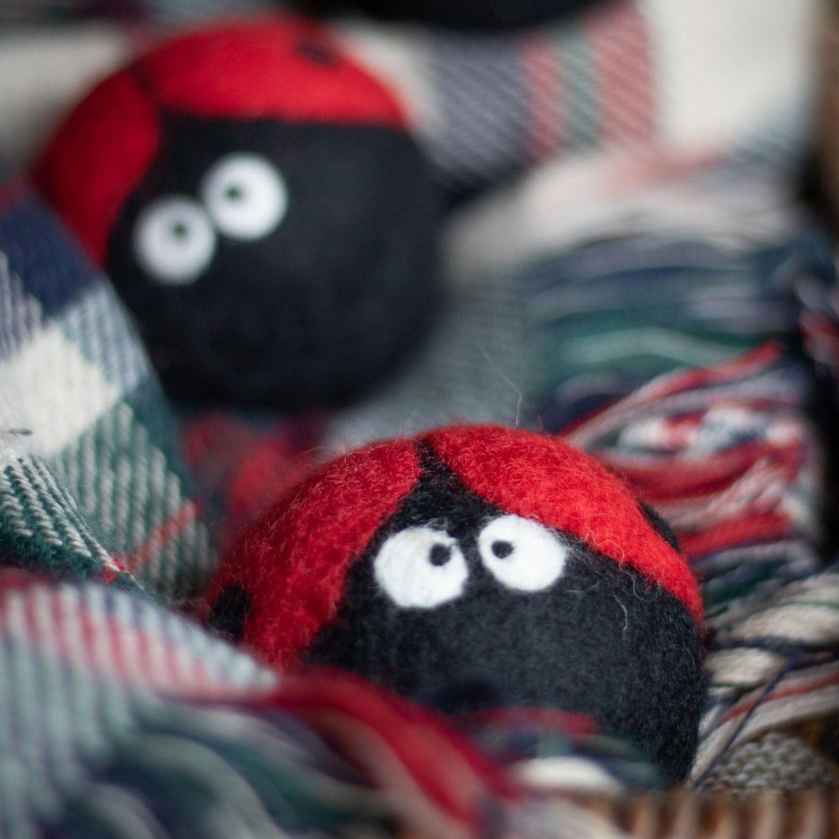 Close-up of plush ladybug dryer ball on plaid blanket, red top and black face