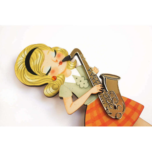 Girl playing saxophone brooch close-up, yellow hair, green top, orange skirt, sax detail.