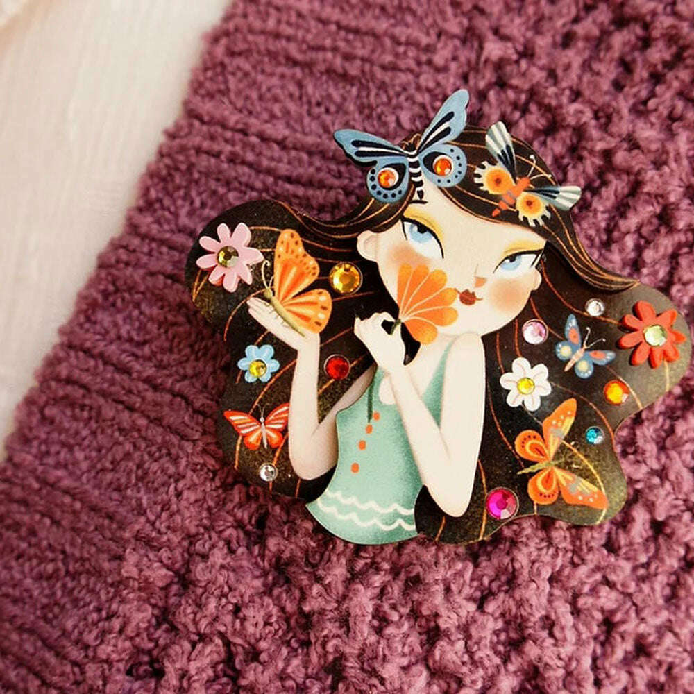Butterfly girl brooch close-up on purple textured fabric, teal dress and flowers