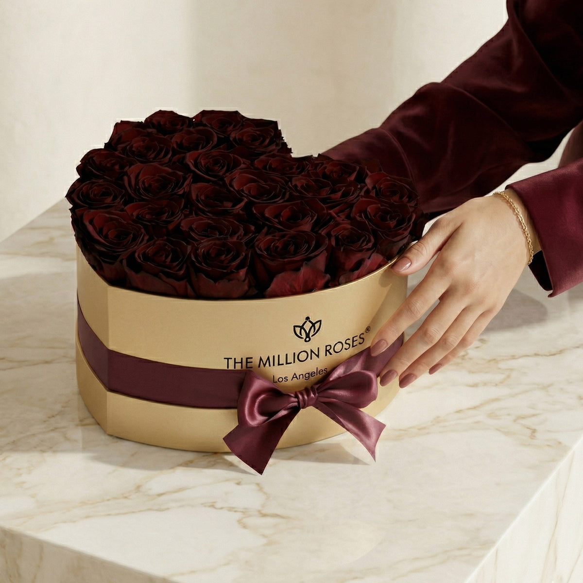 Gold gift box of burgundy roses with satin ribbon bow, hand reaching