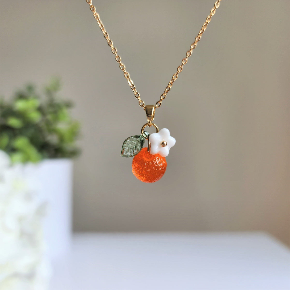 Gold-tone chain necklace with orange fruit charm, white flower, and green leaf