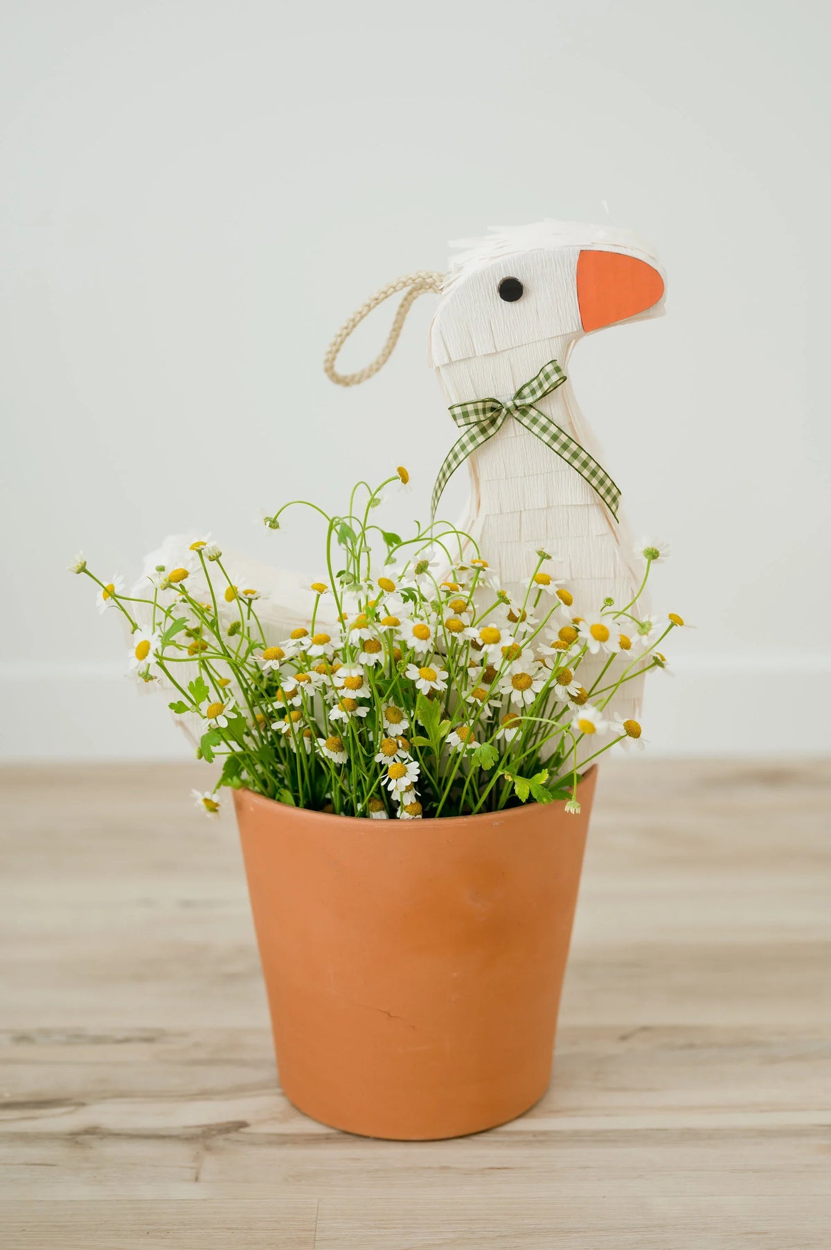 Goose piñata peeking from a terracotta flower pot with daisies