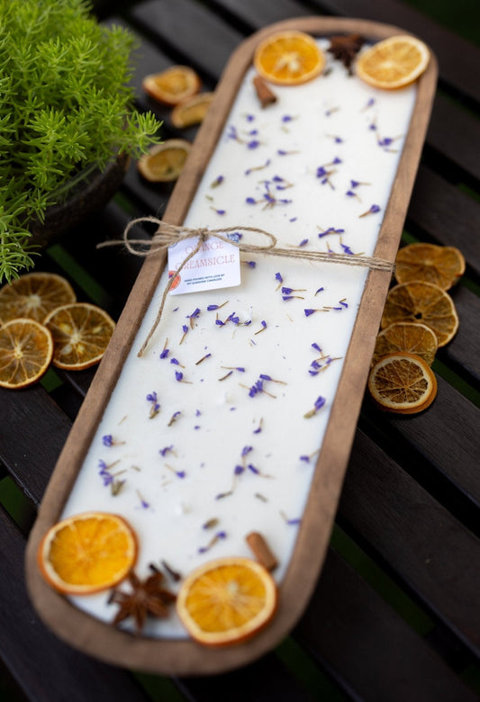 Hand-carved wooden dough bowl candle with white wax, orange citrus slices, and blue lavender sprigs, unlit