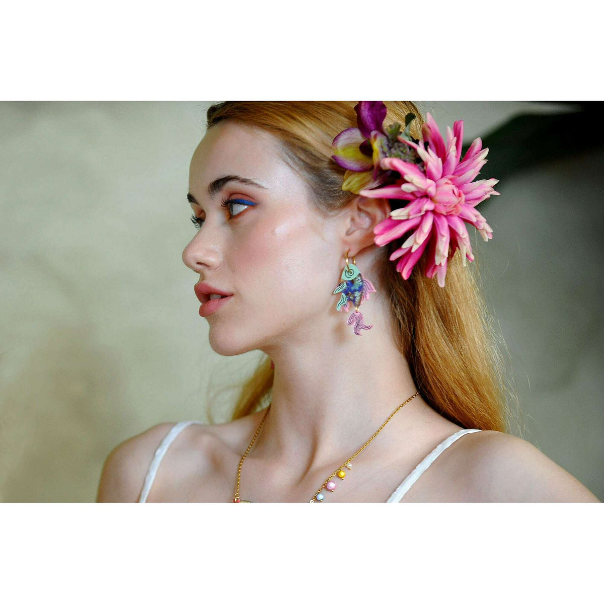 Fish drop earrings with blue, gold, and pink enamel on model profile