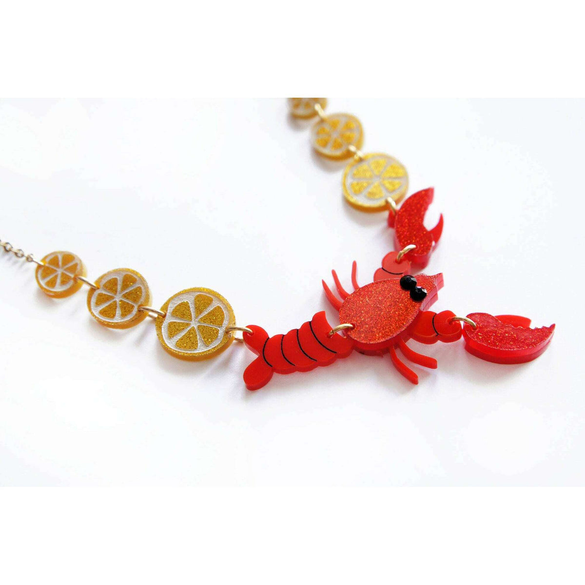 Lobster necklace close-up: gold chain with red lobster and orange slice charms