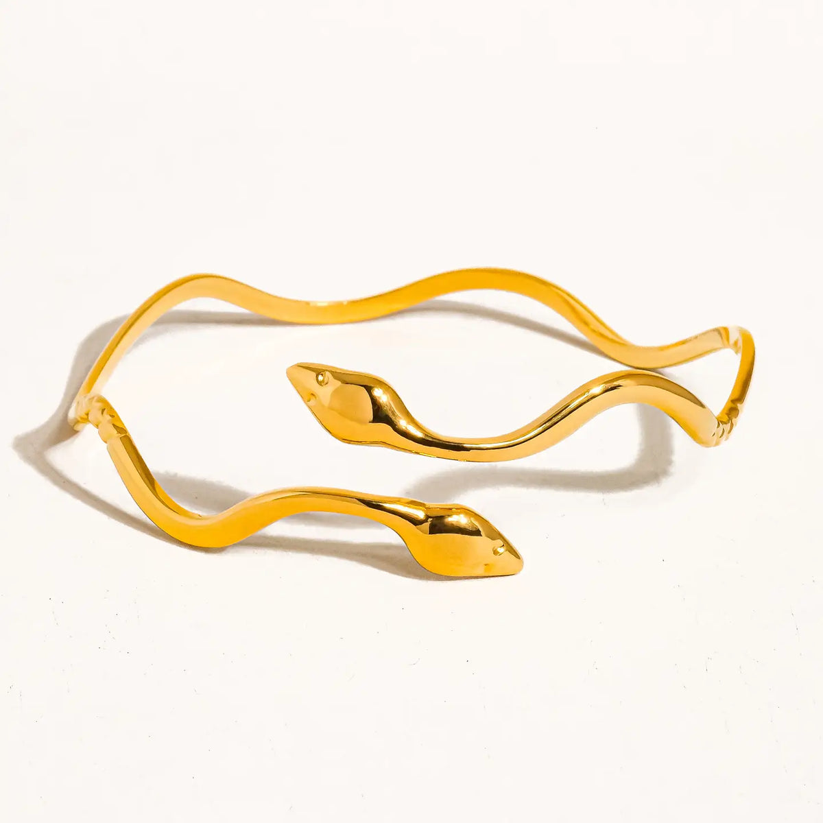 Gold-tone wavy serpent bracelet with two sculpted snake heads