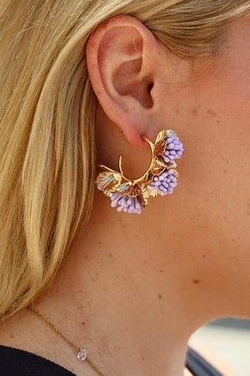 Gold hoop earrings with lavender-purple flower cluster detail near ear