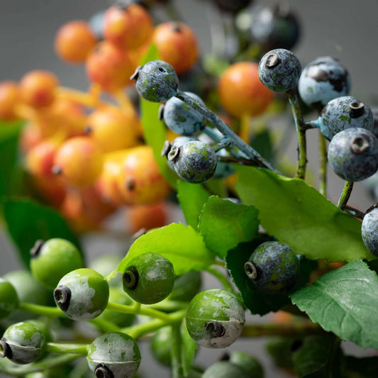 Faux berry stem close-up showing blue, green, and orange berries with leaves