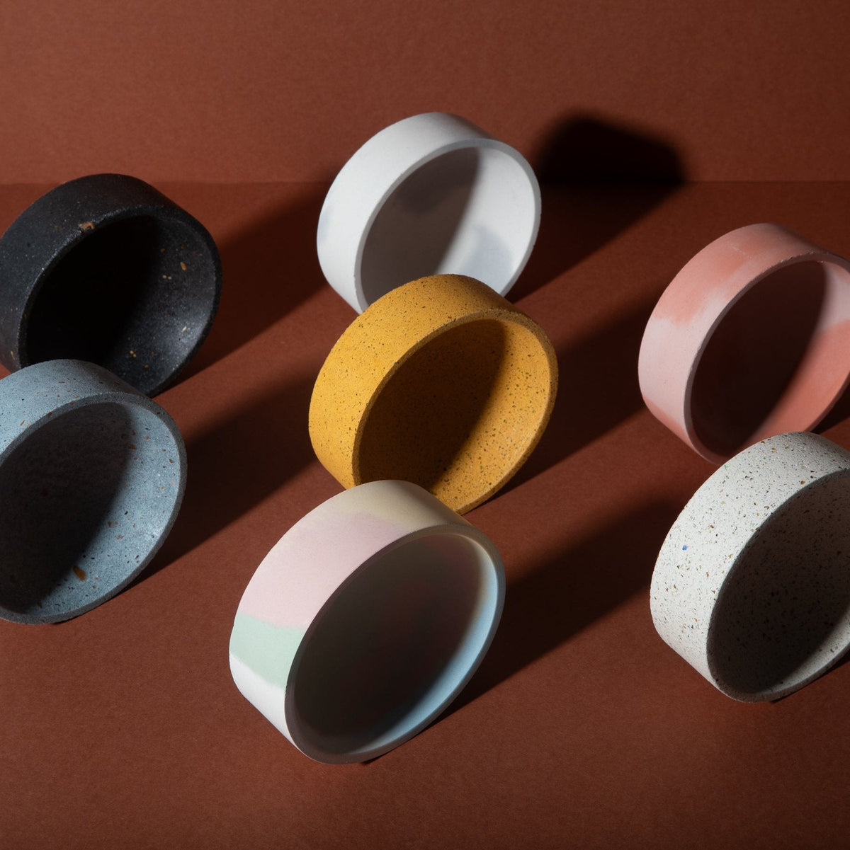 Close-up of round catch-all bowls in black, light blue, yellow, and pink speckled tones.