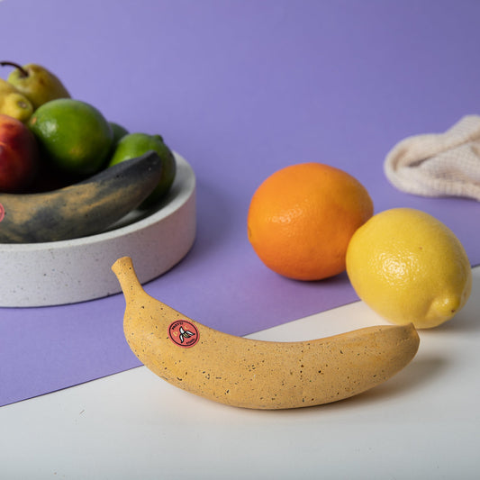 Concrete banana sculpture, yellow speckled finish with small red emblem, on table.