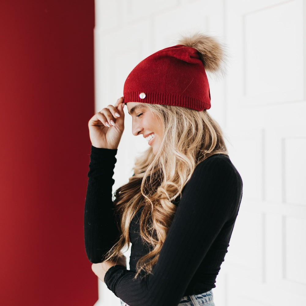 Red knit beanie with fur pom and small metal emblem