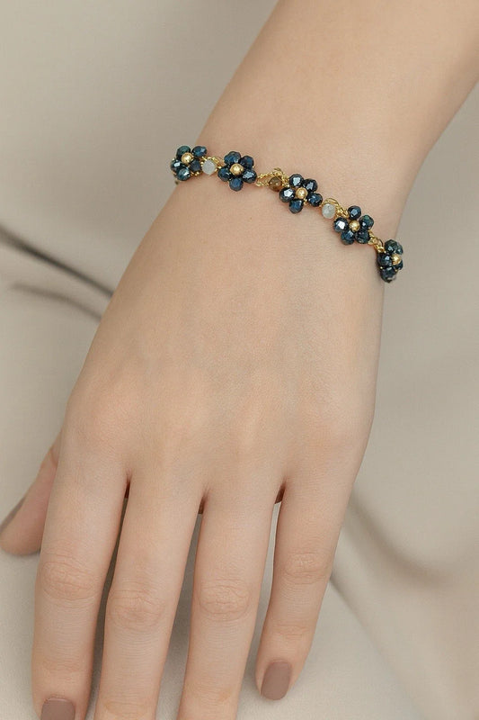 Iridescent floral beaded bracelet on wrist, gold-tone links with dark blue-black beads