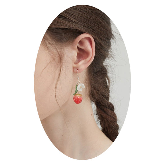 Strawberry and flower drop earrings on ear, with white blooms, green leaves, and red berries