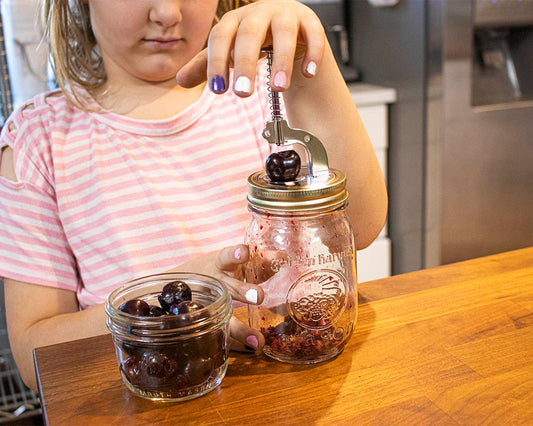 Cherry pitter pressing lever over mason jar filled with cherries