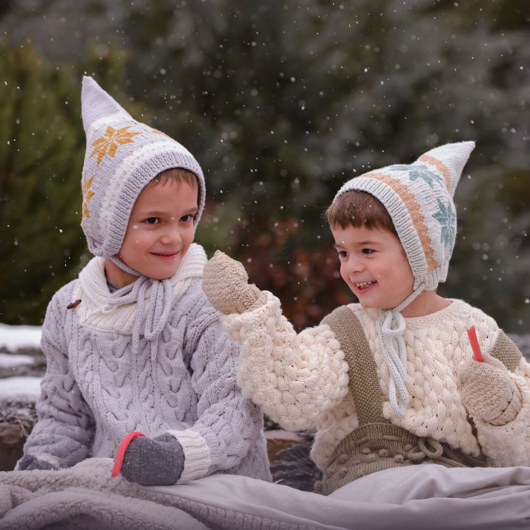 Two knit pixie hats in gray and cream with orange and blue Nordic motifs
