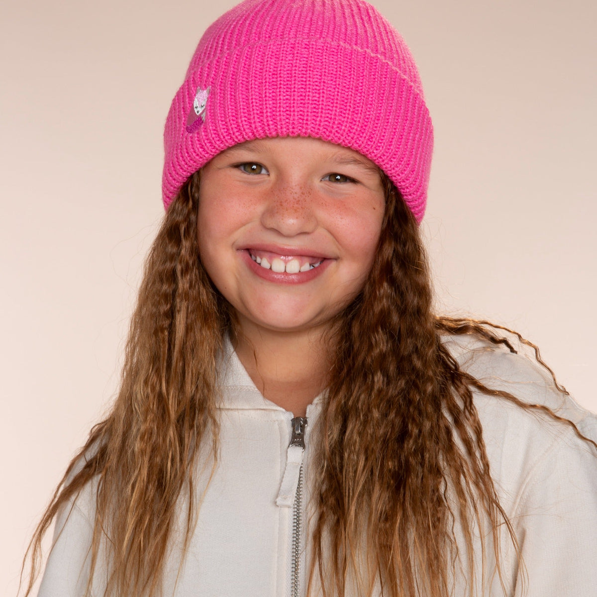 Bright pink knit beanie with a small fox motif, shown worn by a child