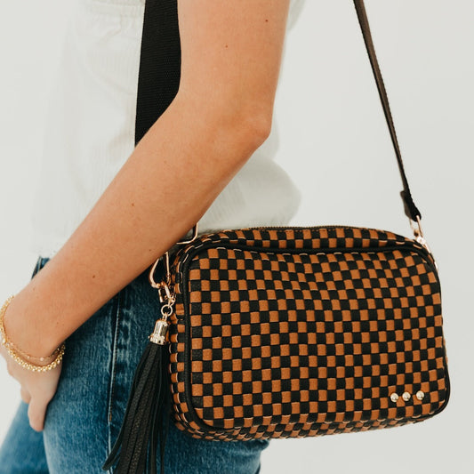 Woven checkered camera crossbody bag in black and brown with long tassel and chain pull.