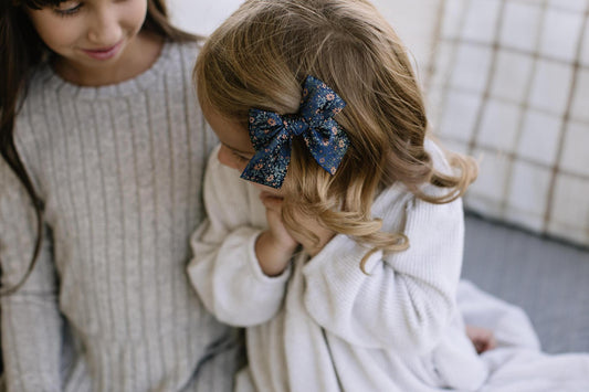 Floral hair bow in dark navy with orange flowers, clipped to a child’s hair.