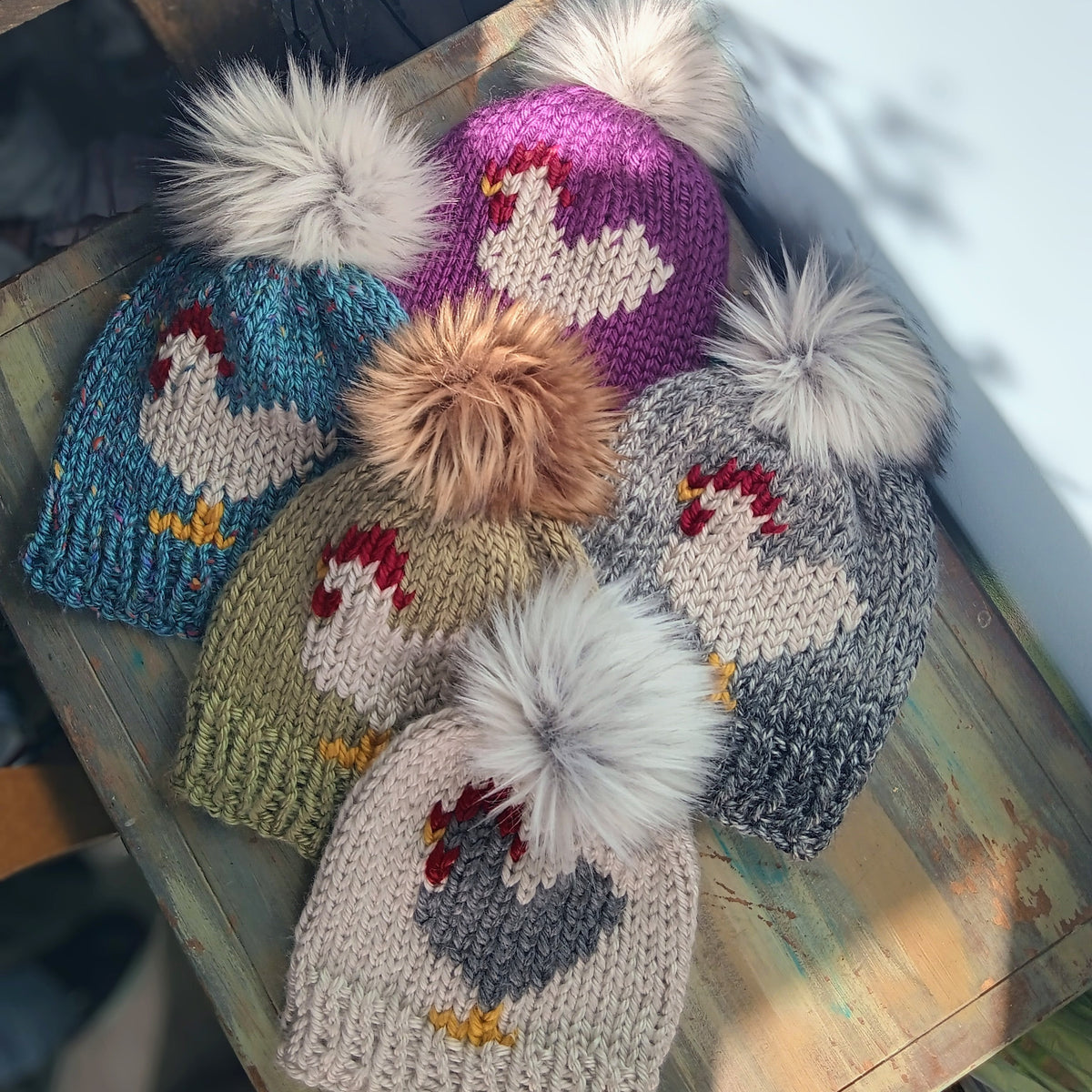 Chicken knit beanie variety, several colors with pom-poms on display