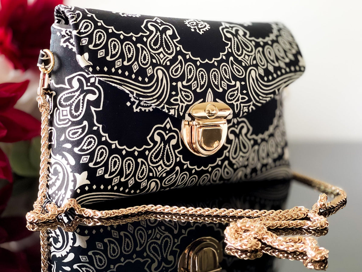 Black bandana print crossbody sling bag with gold-tone front clasp and layered chain strap