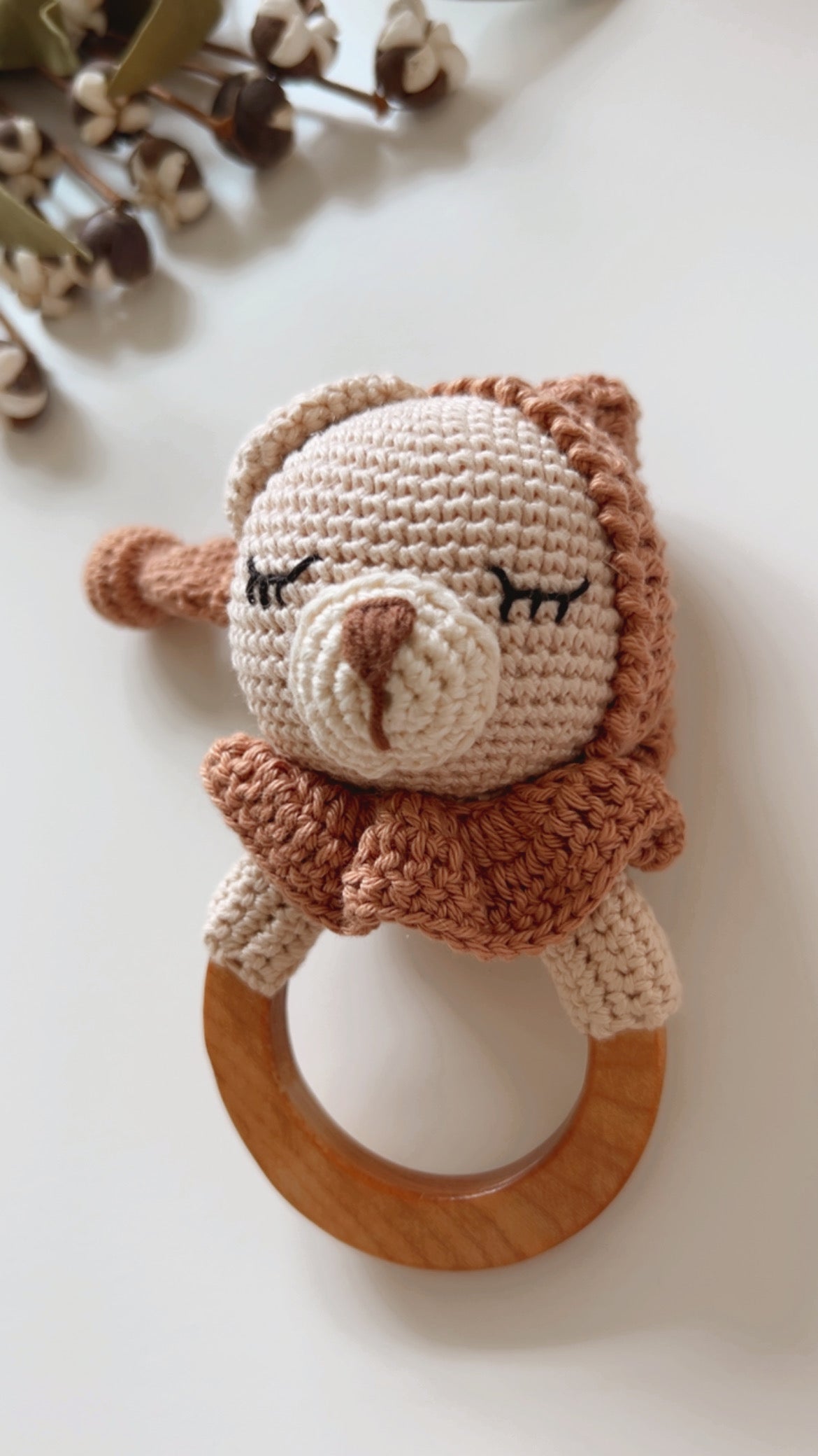 Knitted teddy bear teether rattle with brown-and-beige face and wooden ring, lying