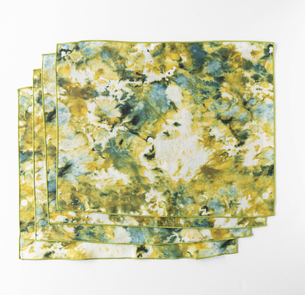 Multiple marble-look placemats stacked, green and yellow pattern with gold-trim edges