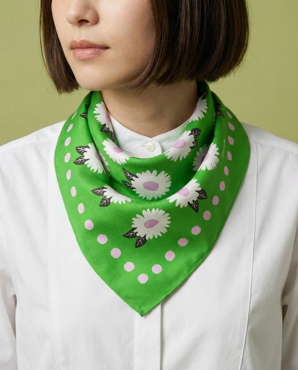Green bandana scarf worn at neck, pink daisy pattern with white dot trim