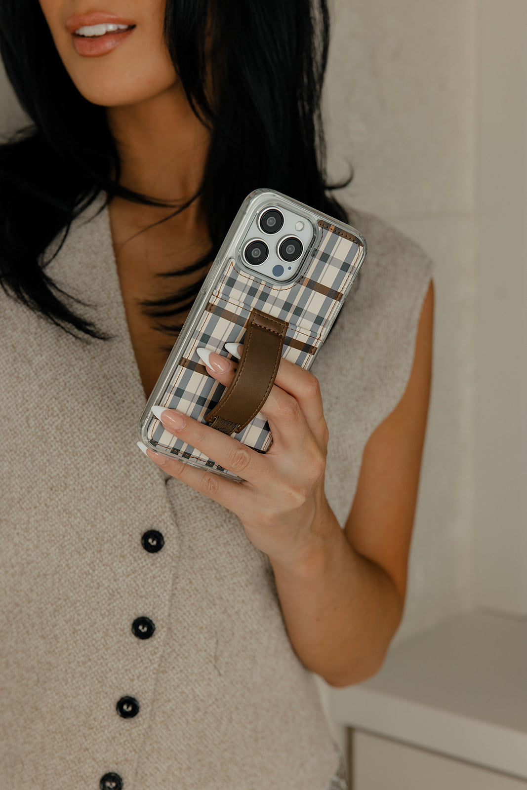 Plaid phone case with brown leather strap on a phone held close-up