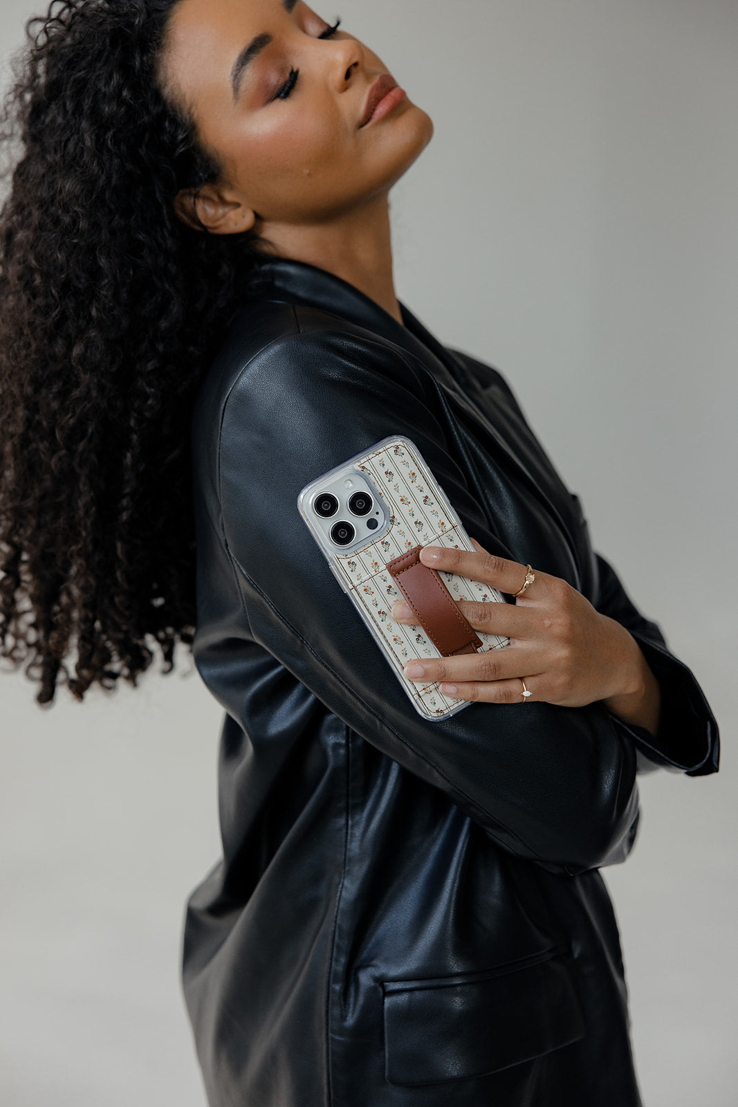 Floral clear phone case with brown leather-style strap, shown in hand