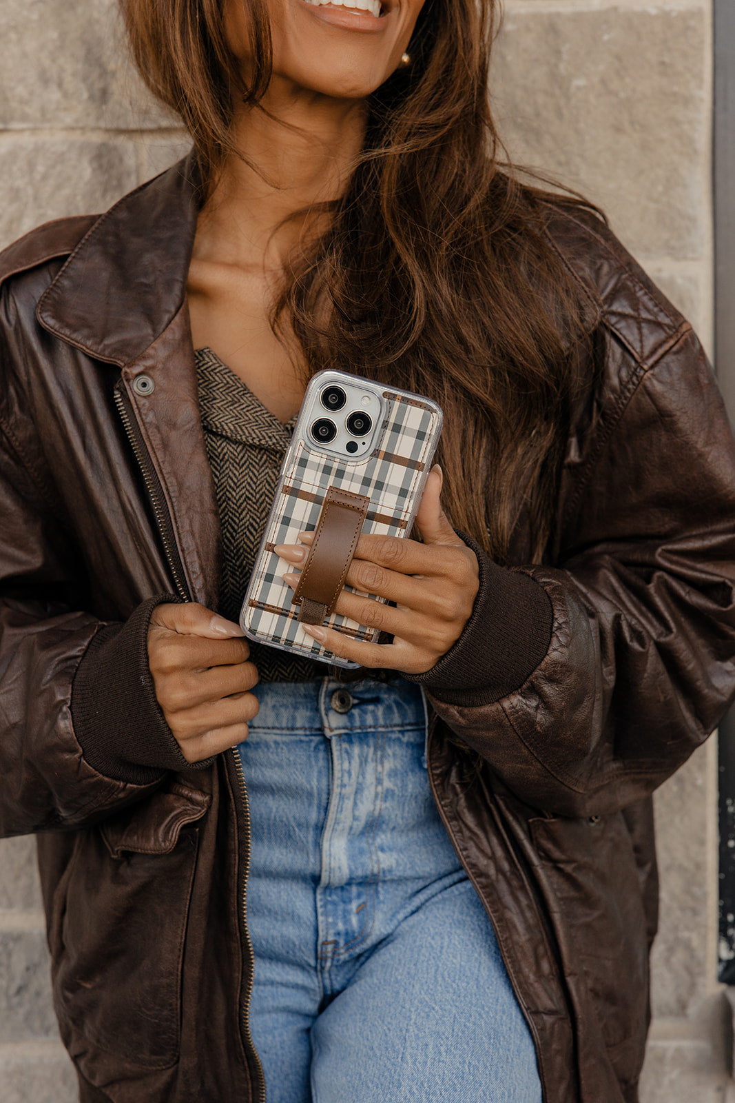 Plaid phone case with brown leather strap held in a hand