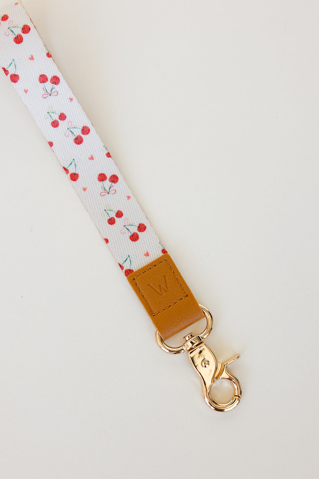 Cherry print wrist lanyard strap with tan leather buckle and gold clasp