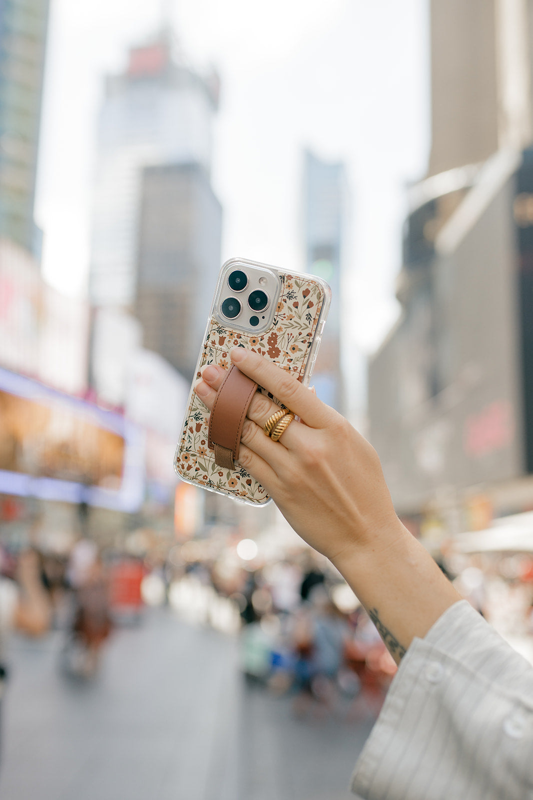 Floral phone case with brown strap pocket on smartphone, held in hand