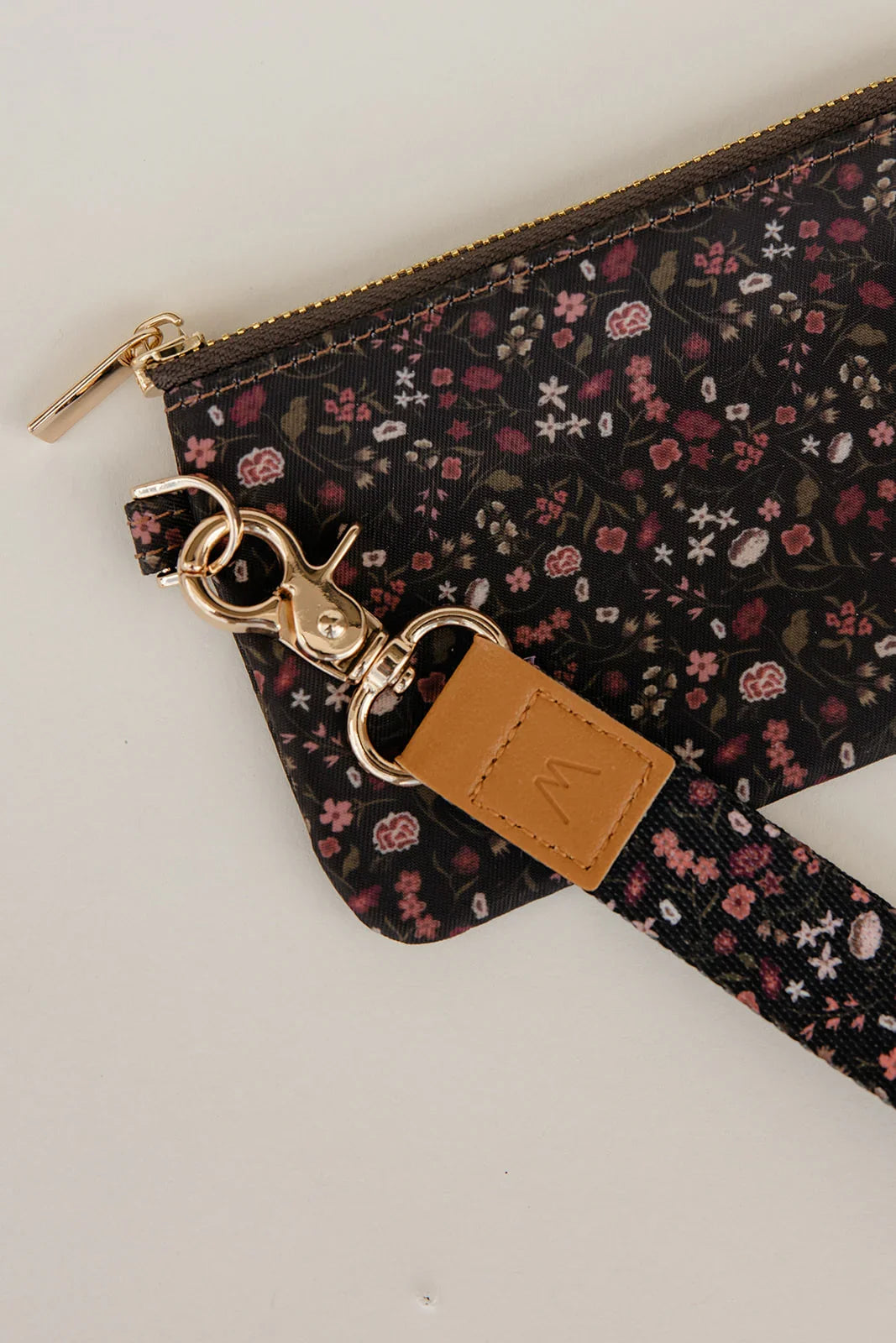 Floral zipper pouch detail with gold pull ring and tan leather accent.