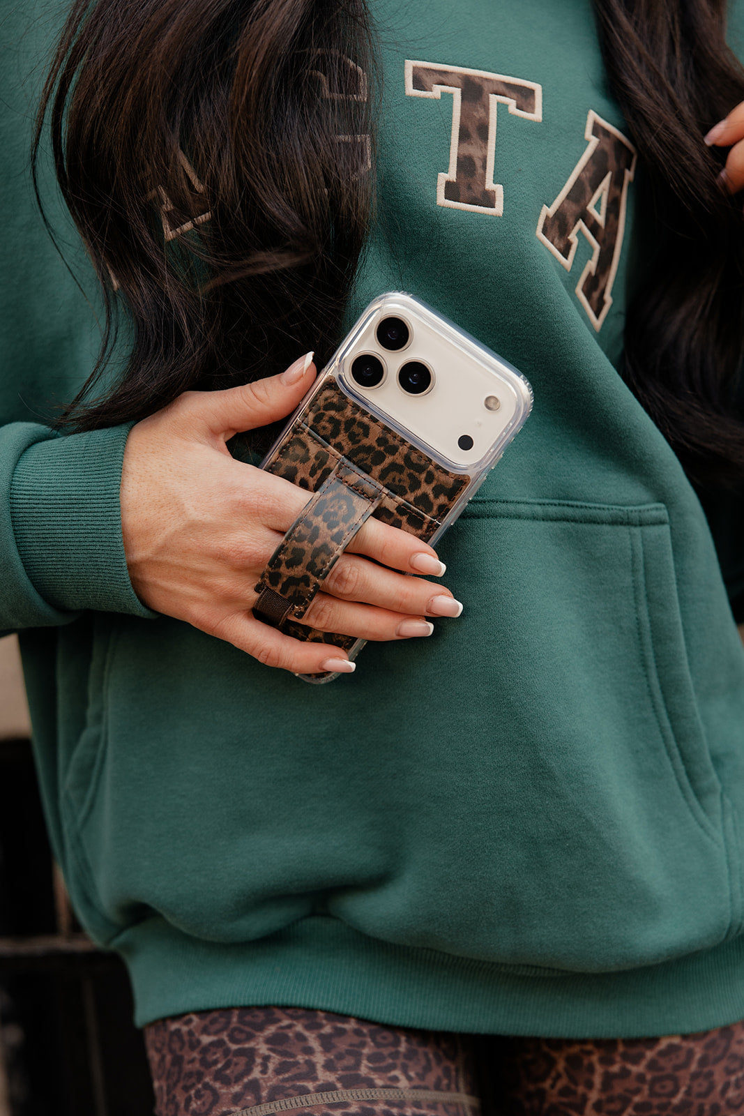 Leopard print phone case with clear back and crossbody-style strap, held in hand