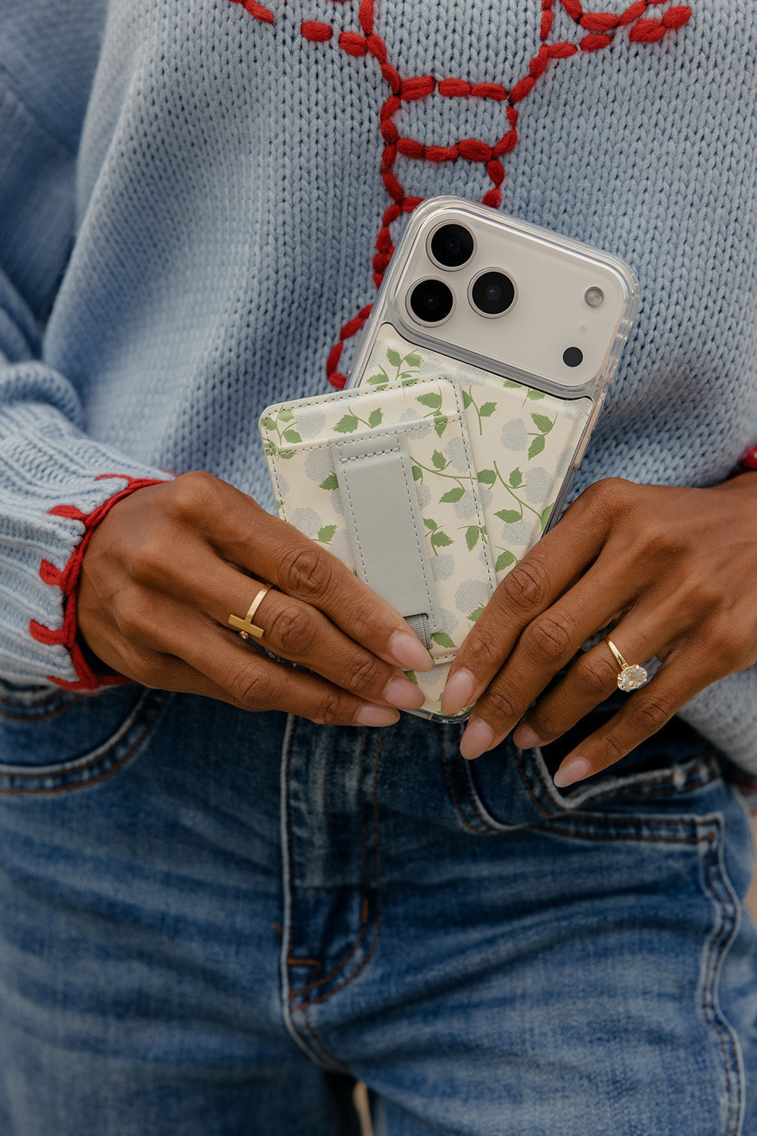 Floral magnetic wallet with gray strap closure held in hands beside a phone