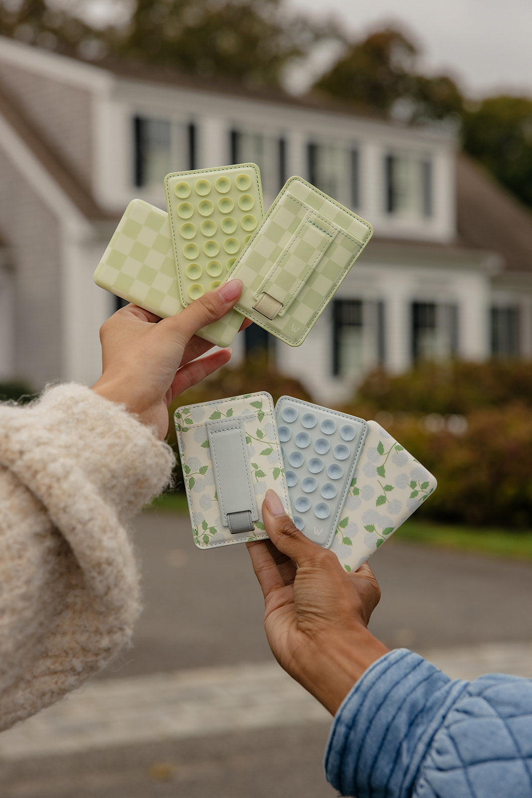 Hands holding several floral magnetic wallets with bubble-texture panels outdoors