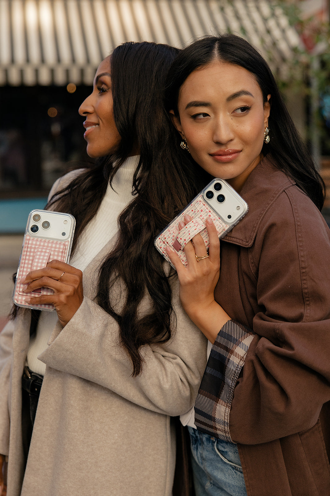Two pastel pink phone cases with clear cutouts and rose-garden designs, held by two people
