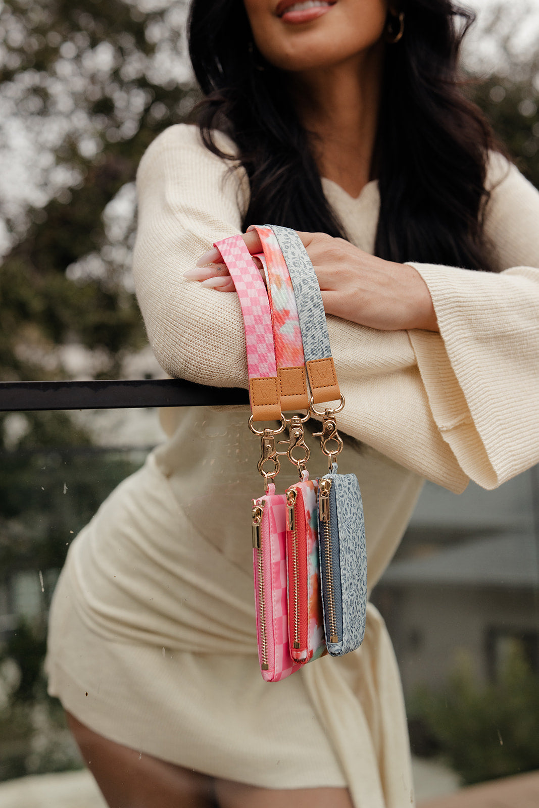 Two small zip pouches with wrist straps—pink check and light blue floral—gold hardware