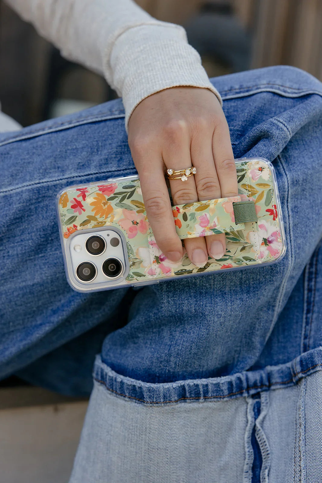Floral phone case with green strap detail on the back, held over blue jeans.