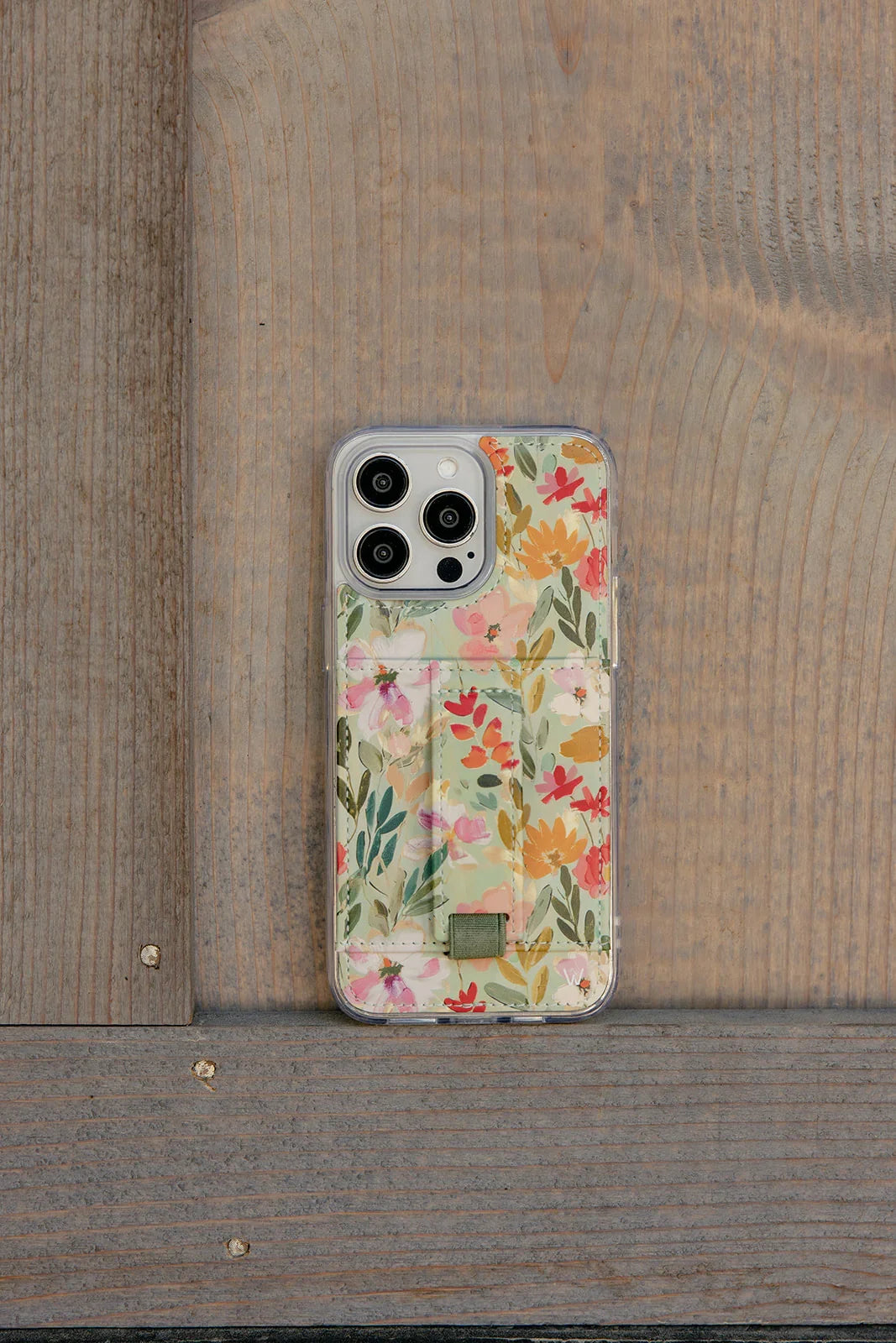 Floral phone case with clear back and green strap, shown on a wood surface.