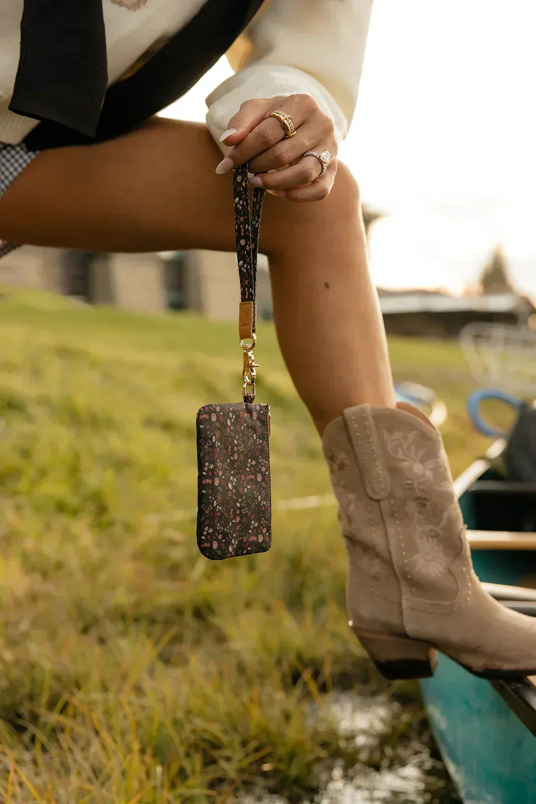 Floral wrist lanyard with zip pouch hanging from wrist, gold hardware and brown strap