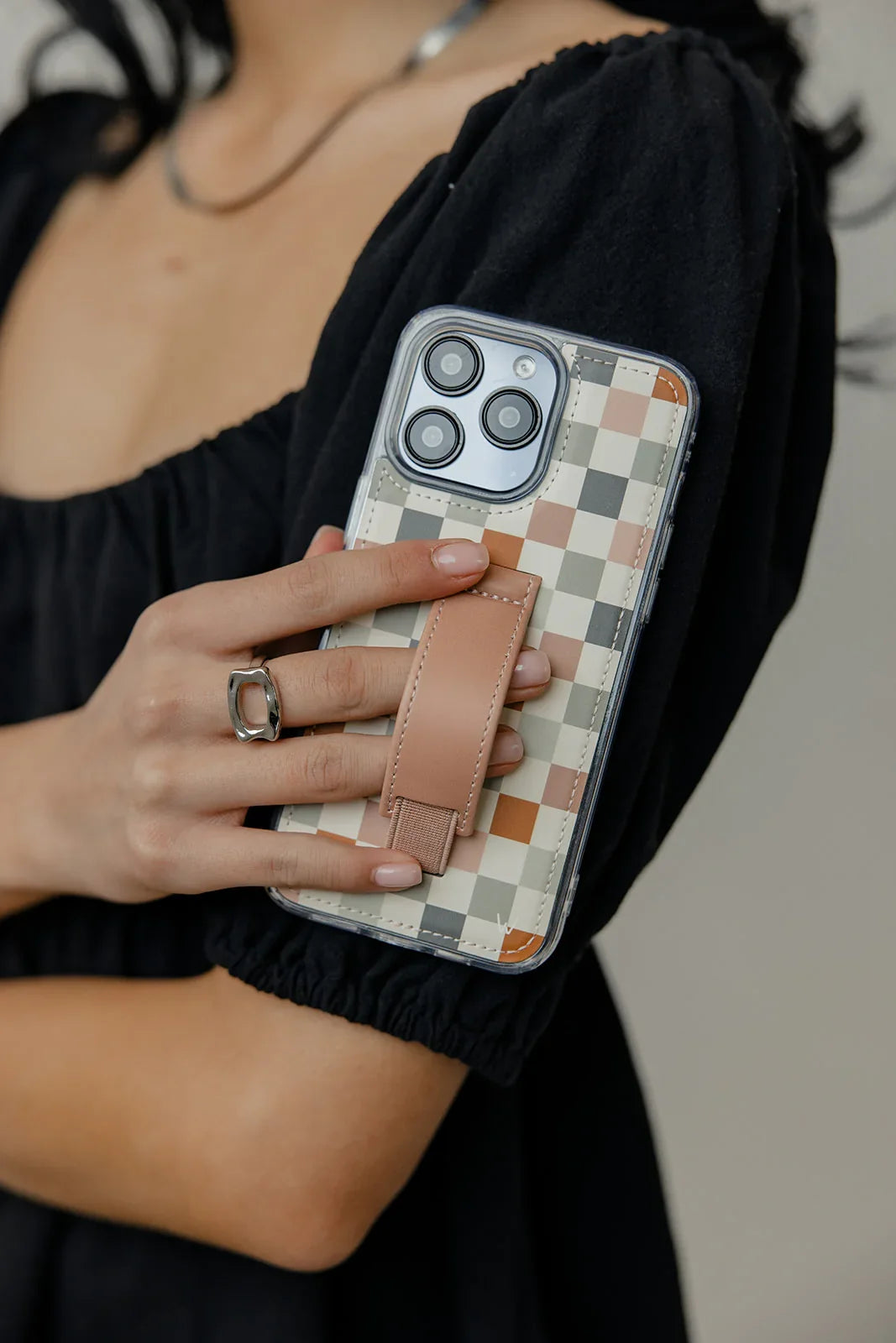 Phone case with multicolor check design and tan strap, held by person