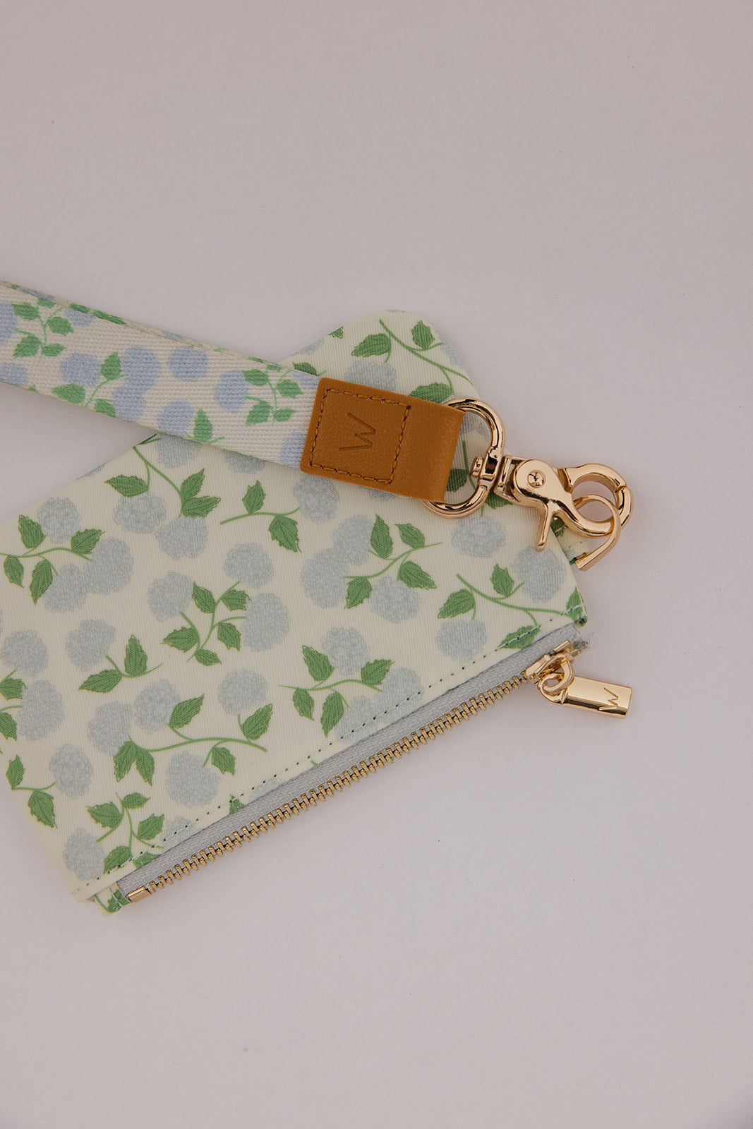 Leaf-print wrist lanyard with tan leather tag, clasp, and zipper pouch