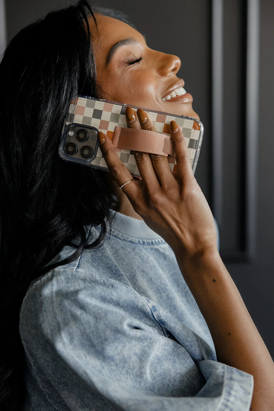 Check pattern phone case with tan strap, held near face with smile